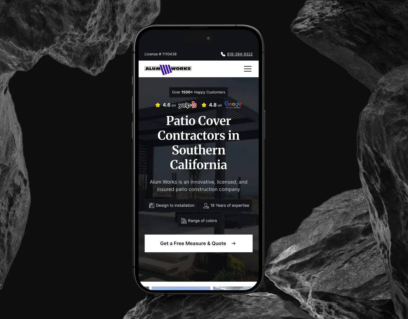 The Alum Works mobile homepage on an iPhone set upright between dark rocks — the Patio Cover Contractors in Southern California hero with its Yelp and Google ratings.