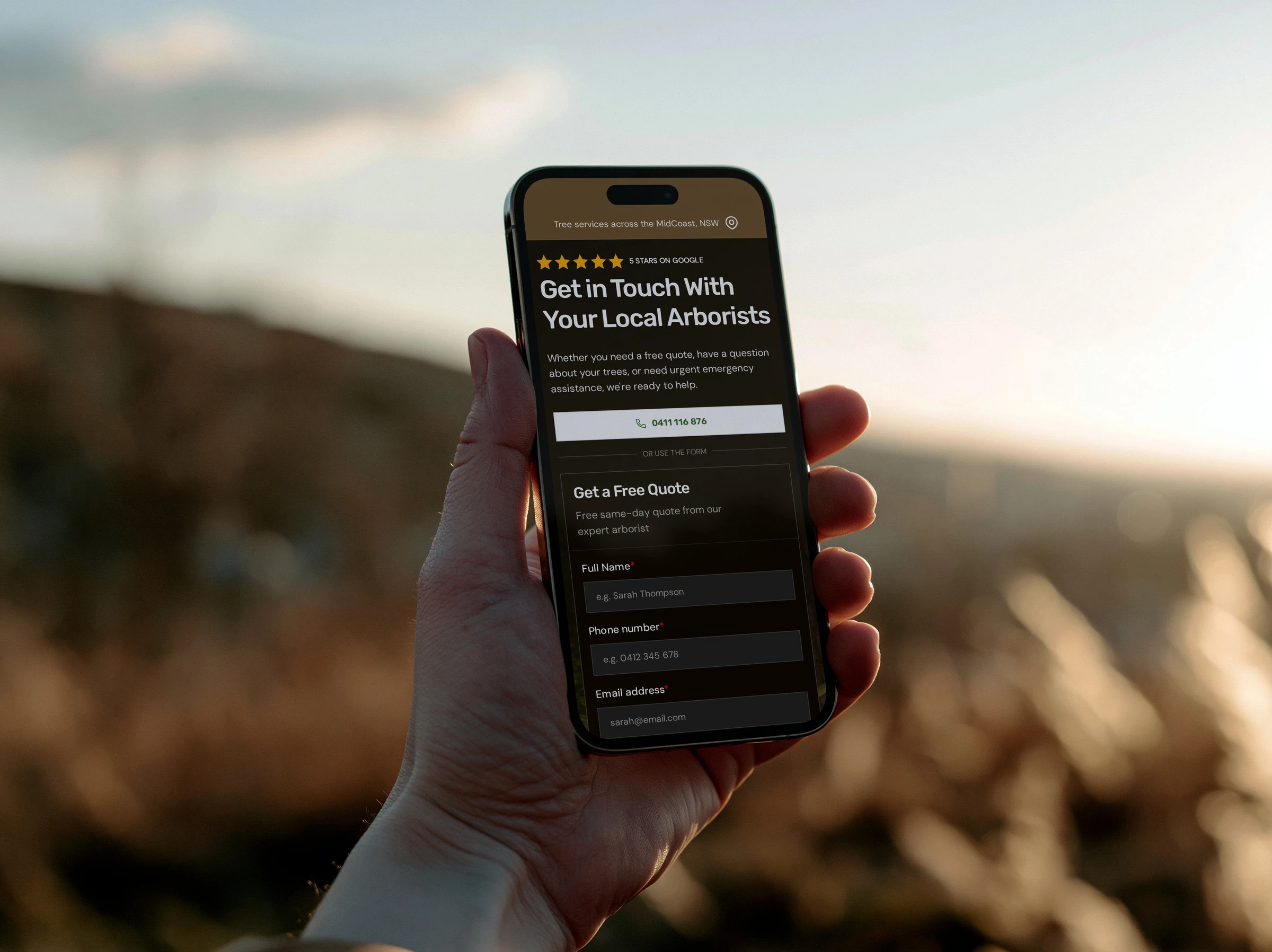 The MidCoast Tree Solutions contact page on a phone held up outdoors at sunset: Get in Touch With Your Local Arborists, above the phone button and quote form