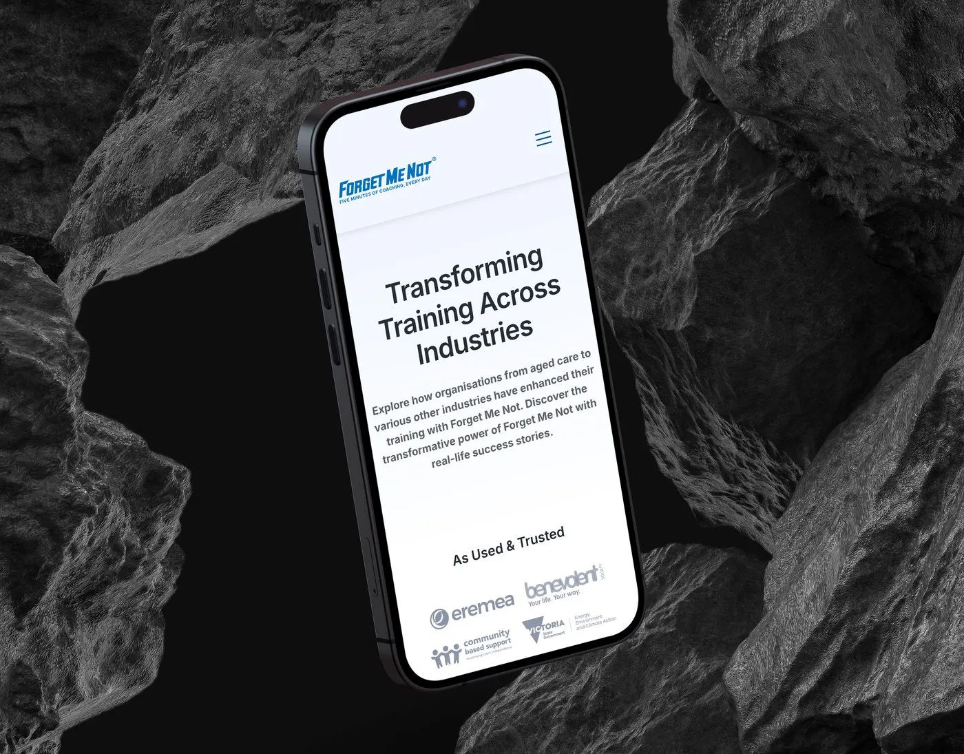 The Forget Me Not® success-stories page on an iPhone angled among dark volcanic rocks — Transforming Training Across Industries above its As Used & Trusted logo row.