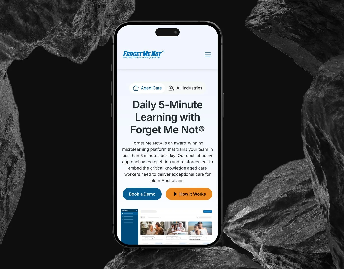 The Forget Me Not® mobile homepage on an iPhone set upright between dark rocks — Daily 5-Minute Learning with Forget Me Not® above the Book a Demo button.