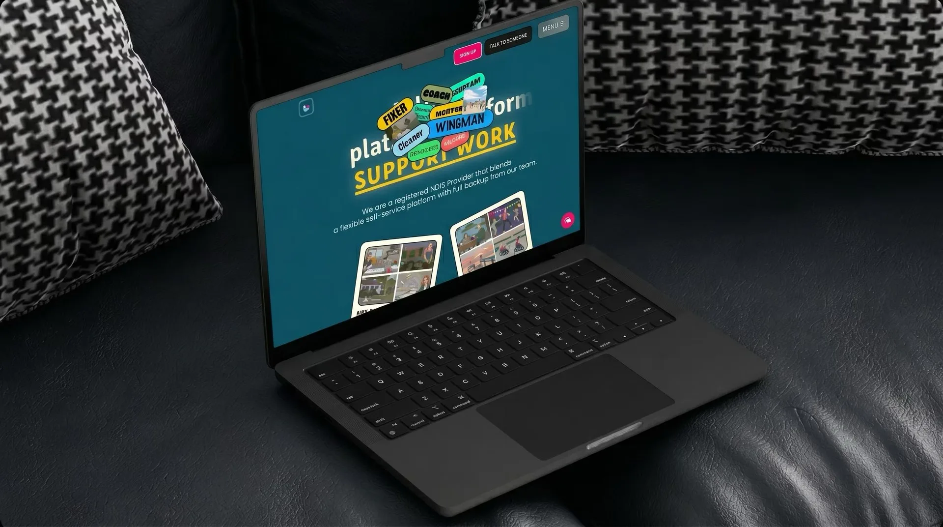 The Humdrum homepage open on a MacBook resting on a dark leather sofa, its teal hero showing the underlined SUPPORT WORK headline behind a cluster of role tags — Fixer, Coach, Wingman, Cleaner — above the registered NDIS Provider intro line.
