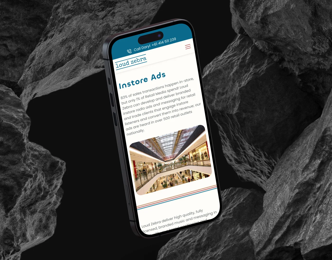 The Loud Zebra in-store audio page on an iPhone angled among dark volcanic rocks, headed "Instore Ads" above a photo of a shopping centre.