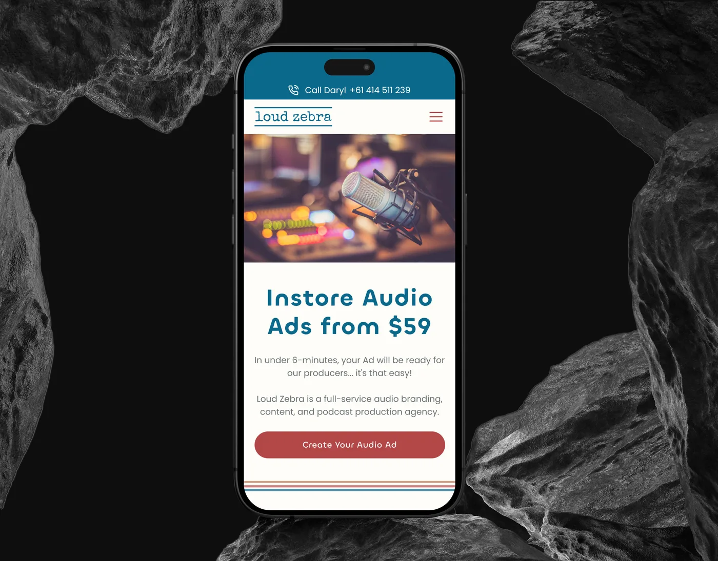 The Loud Zebra mobile homepage on an iPhone set upright between dark rocks: a studio microphone above "Instore Audio Ads from $59" and the Create Your Audio Ad button.