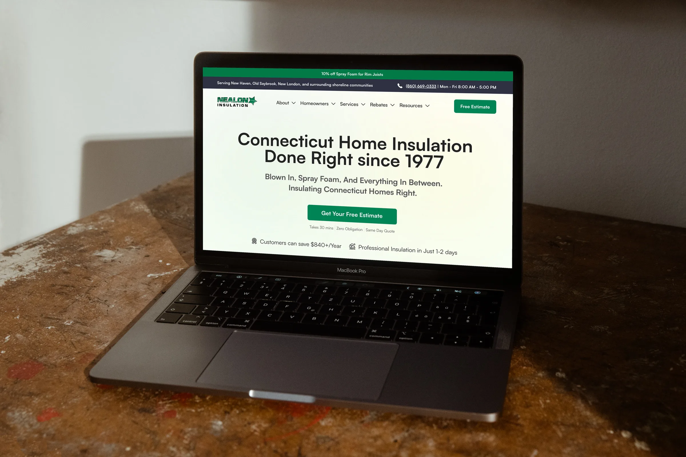 The Nealon Insulation homepage on a MacBook Pro on a worn timber workbench — the "Connecticut Home Insulation Done Right since 1977" hero with its green Get Your Free Estimate button and savings badges.